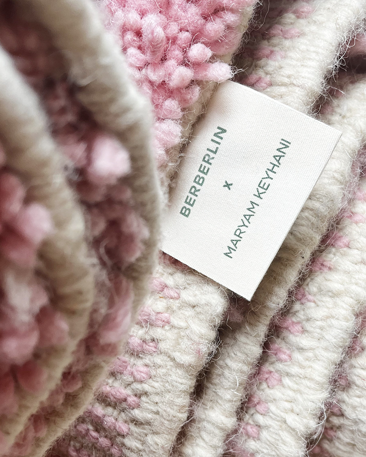 Cotton cream label with Berberlin x Maryam Keyhani printed in green and hand-stitched onto a pink, cream and burgundy wool berber rug.